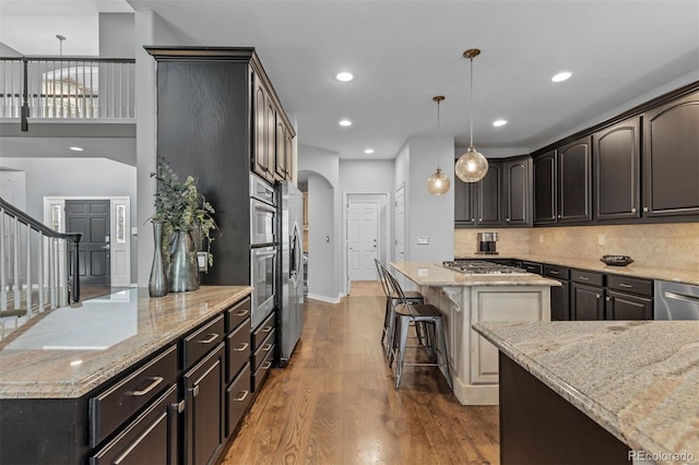kitchen featuring dark wood-style flooring, stainless steel appliances, a center island, and light stone countertops