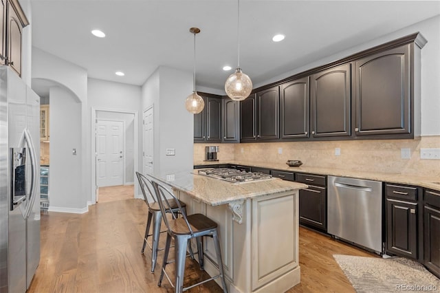 kitchen featuring appliances with stainless steel finishes, a breakfast bar area, a center island, light stone counters, and light wood-type flooring