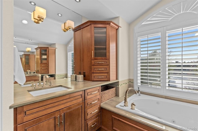 full bathroom with lofted ceiling, a tub with jets, a healthy amount of sunlight, and vanity