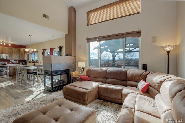 living room featuring visible vents, an inviting chandelier, a high ceiling, light wood-type flooring, and a fireplace