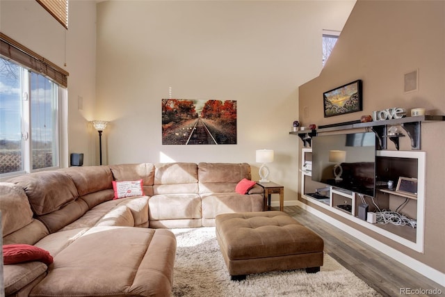 living area featuring a high ceiling, baseboards, and wood finished floors