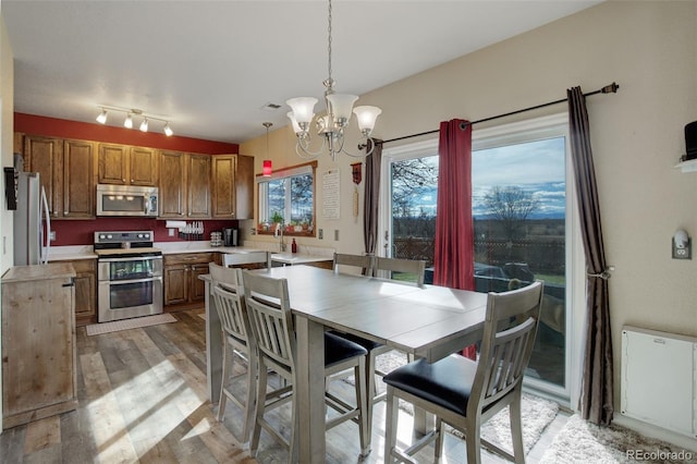 kitchen with brown cabinets, a notable chandelier, stainless steel appliances, light countertops, and light wood-type flooring