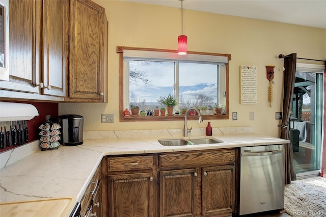 kitchen with brown cabinetry, decorative light fixtures, a sink, and stainless steel dishwasher