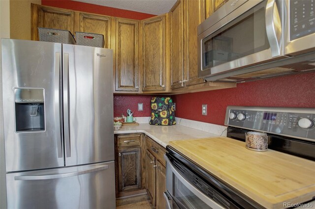 kitchen with stainless steel appliances, brown cabinetry, and wooden counters