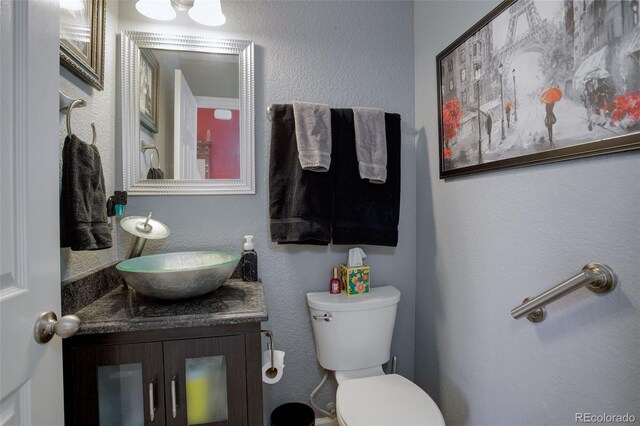 half bathroom featuring toilet, a textured wall, and vanity