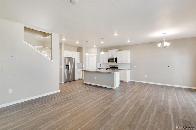 kitchen with appliances with stainless steel finishes, white cabinetry, sink, hanging light fixtures, and a center island with sink