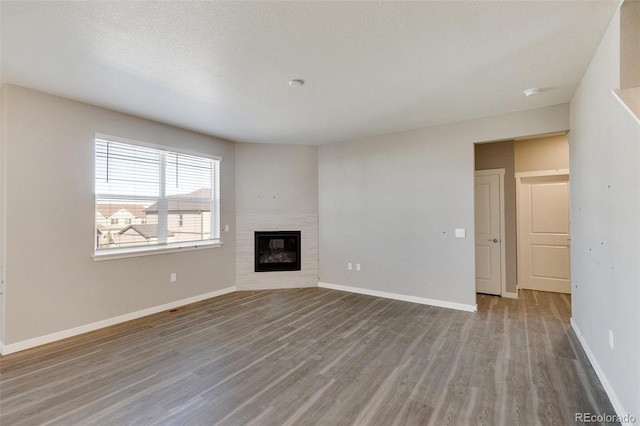 unfurnished living room featuring a tiled fireplace, hardwood / wood-style floors, and a textured ceiling