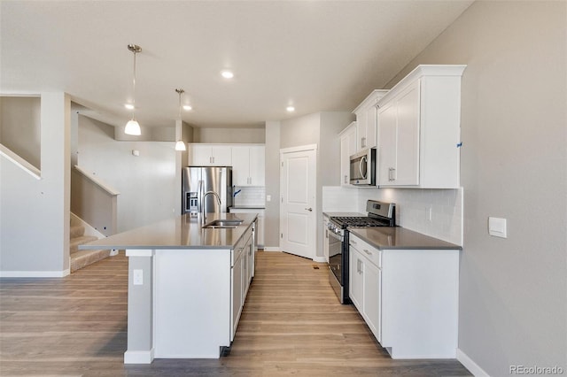 kitchen featuring appliances with stainless steel finishes, decorative light fixtures, white cabinetry, an island with sink, and sink