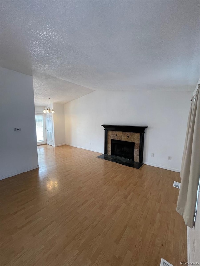 unfurnished living room featuring a notable chandelier, light hardwood / wood-style floors, and a textured ceiling