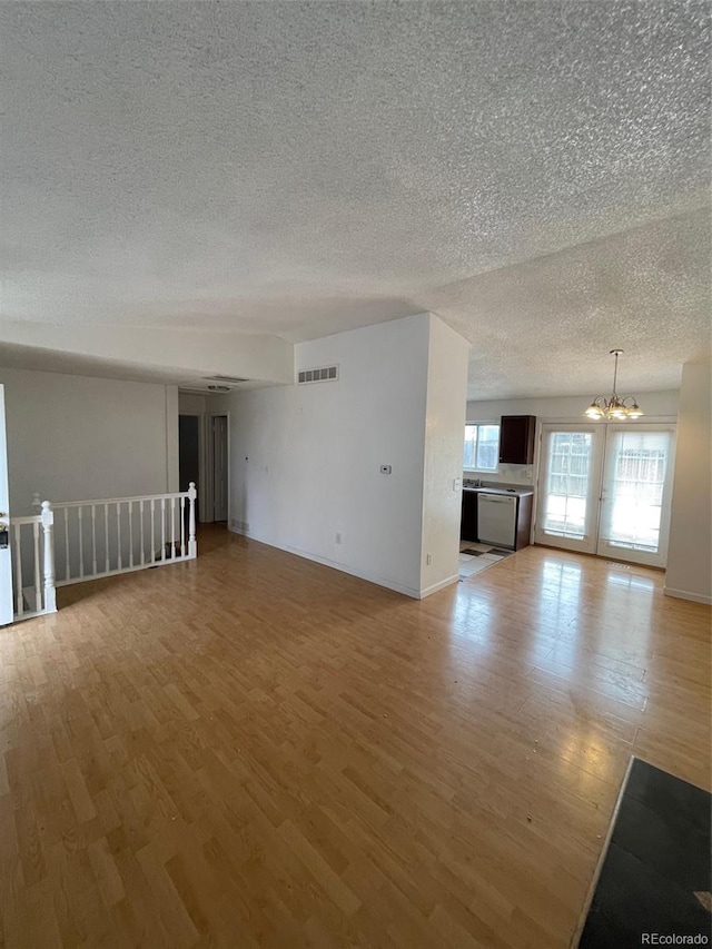 empty room featuring a textured ceiling, wood-type flooring, and an inviting chandelier