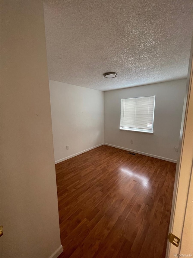 empty room with a textured ceiling and dark hardwood / wood-style floors