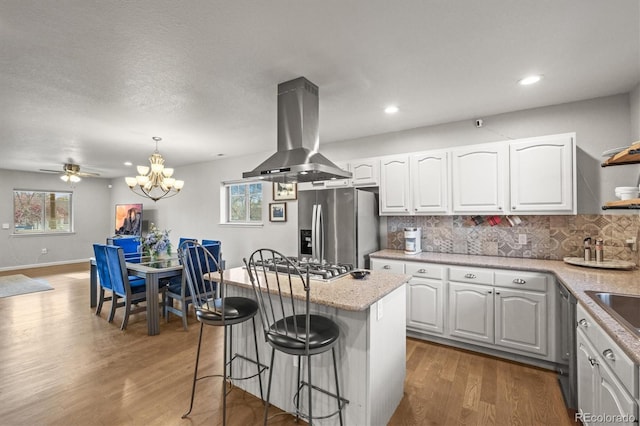 4942 Grove St, Denver, CO 80221 - kitchen with white cabinets, wood finished floors, island exhaust hood, and appliances with stainless steel finishes