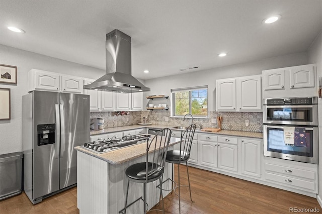 4942 Grove St, Denver, CO 80221 - kitchen with a kitchen bar, stainless steel appliances, island range hood, white cabinets, and backsplash