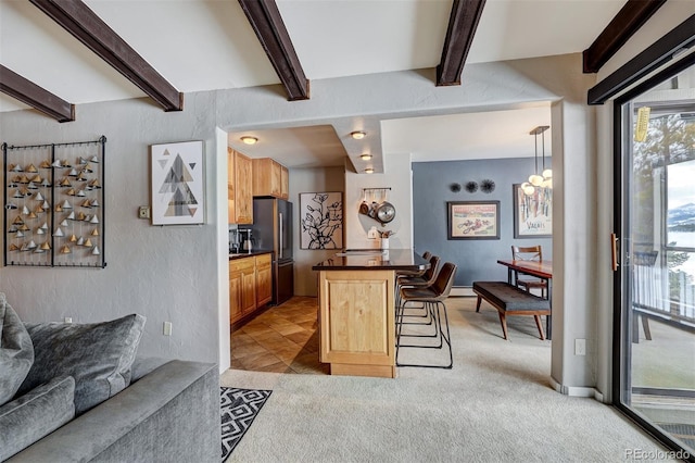 kitchen with a breakfast bar area, light carpet, stainless steel fridge, kitchen peninsula, and beamed ceiling