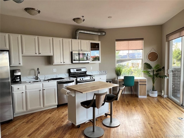 1441 Central Unit 305, Denver, CO 80211 - kitchen with appliances with stainless steel finishes, wood counters, light wood-style floors, white cabinets, and a kitchen bar