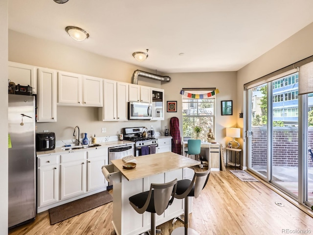 1441 Central Unit 305, Denver, CO 80211 - kitchen with appliances with stainless steel finishes, light wood finished floors, white cabinetry, and a breakfast bar
