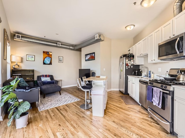 1441 Central Unit 305, Denver, CO 80211 - kitchen with appliances with stainless steel finishes, white cabinetry, light wood-type flooring, and a breakfast bar area