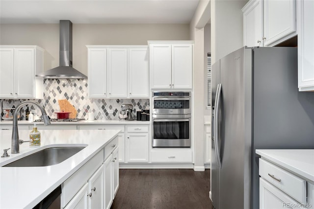 kitchen with sink, dark wood-type flooring, white cabinetry, stainless steel appliances, and wall chimney exhaust hood