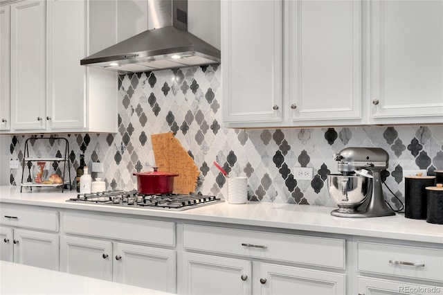 kitchen featuring wall chimney exhaust hood, stainless steel gas cooktop, decorative backsplash, and white cabinets