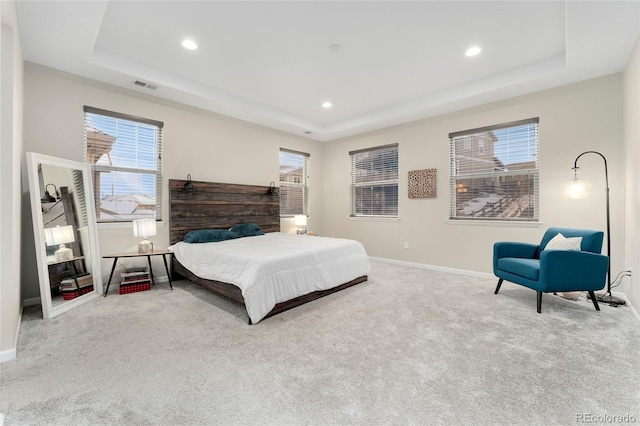 bedroom featuring multiple windows, light carpet, and a tray ceiling