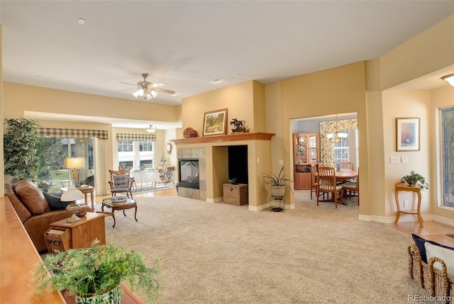 carpeted living area featuring baseboards, a tile fireplace, and ceiling fan with notable chandelier