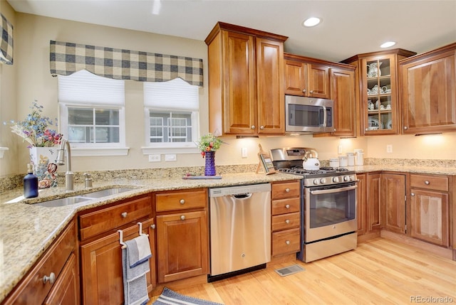 kitchen featuring a sink, light wood-style flooring, light stone counters, and stainless steel appliances