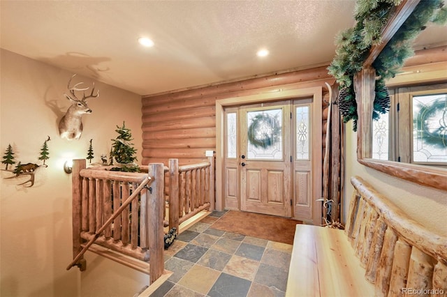 foyer featuring a wealth of natural light, stone finish floor, log walls, and a textured ceiling