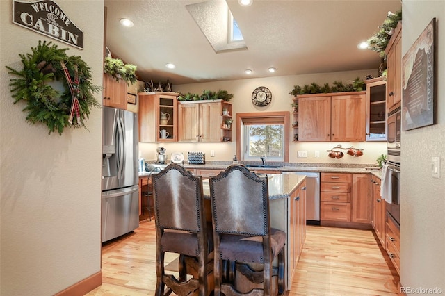 kitchen featuring light wood finished floors, glass insert cabinets, appliances with stainless steel finishes, a kitchen bar, and open shelves