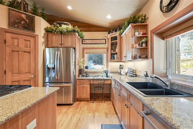 kitchen with light stone counters, appliances with stainless steel finishes, glass insert cabinets, vaulted ceiling, and a sink