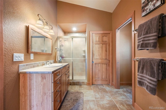 bathroom with a stall shower, vaulted ceiling, vanity, and baseboards