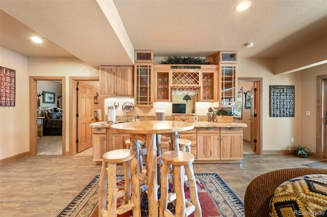 kitchen with baseboards, glass insert cabinets, light countertops, a textured ceiling, and light brown cabinets