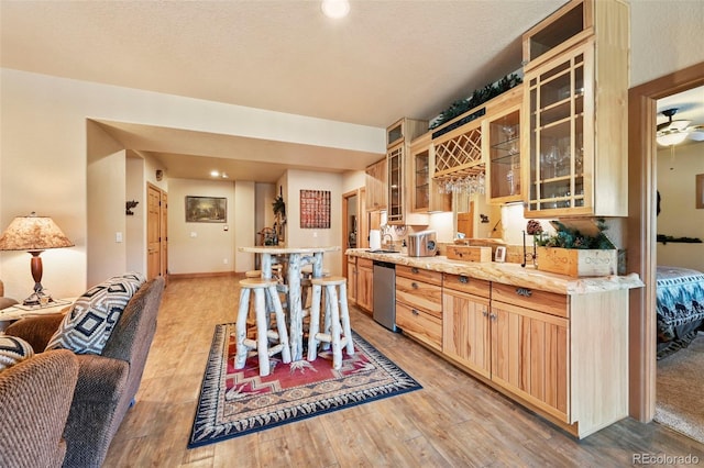 kitchen with light countertops, stainless steel dishwasher, light brown cabinetry, light wood finished floors, and glass insert cabinets