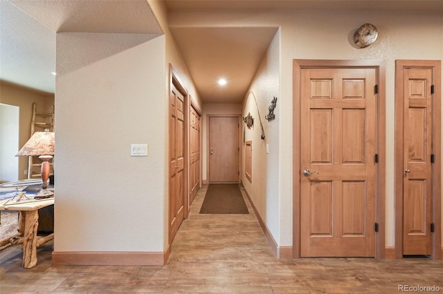 corridor with a textured wall, light wood-type flooring, and baseboards