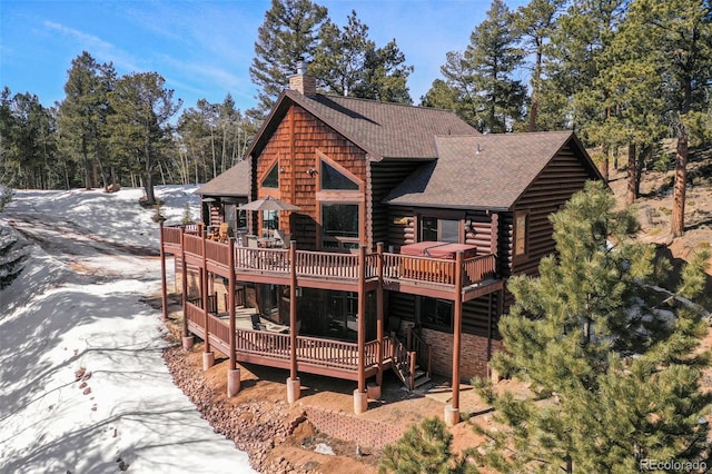 back of property with a shingled roof, a chimney, and a deck