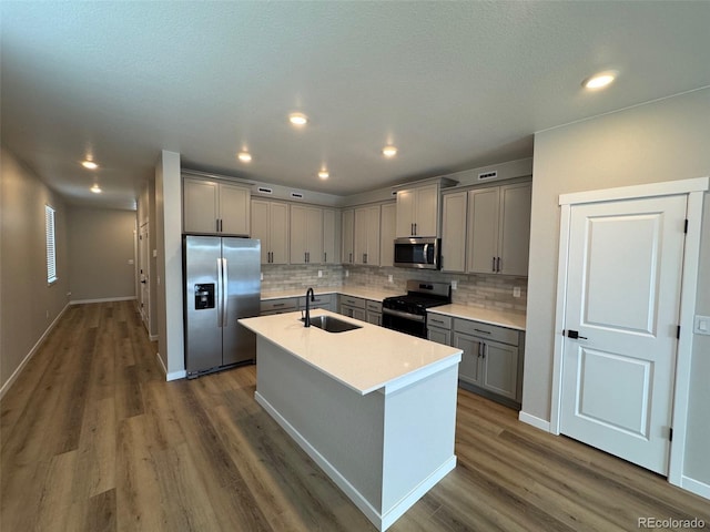 kitchen with dark wood-type flooring, gray cabinets, a sink, backsplash, and stainless steel appliances