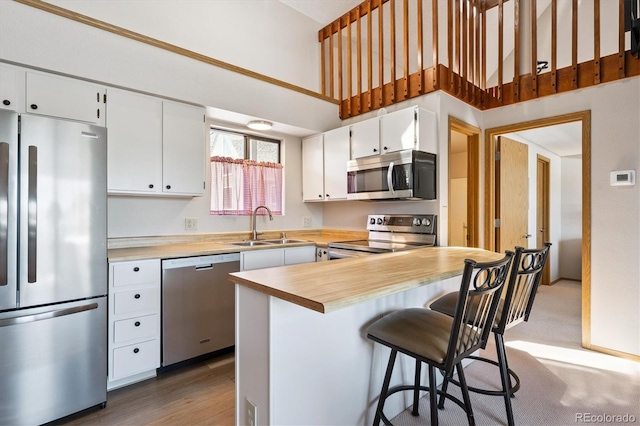 5250 S Huron Way Unit 5-308, Littleton, CO 80120 - kitchen featuring appliances with stainless steel finishes, a high ceiling, white cabinetry, a kitchen bar, and butcher block counters