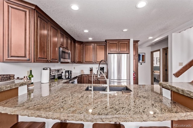 20223 Goins Dr, Morrison, CO 80465 - kitchen featuring stainless steel appliances, recessed lighting, a peninsula, light stone countertops, and a kitchen bar