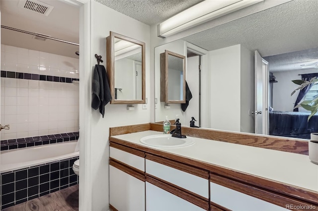 bathroom with toilet, tiled shower / bath combo, a textured ceiling, visible vents, and vanity