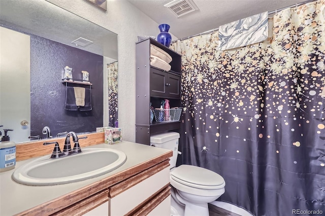 full bath with vanity, toilet, a textured wall, and visible vents