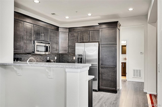 3437 Rosato Dr Unit C, Highlands Ranch, CO 80126 - kitchen with appliances with stainless steel finishes, dark brown cabinetry, a kitchen bar, light wood finished floors, and a peninsula