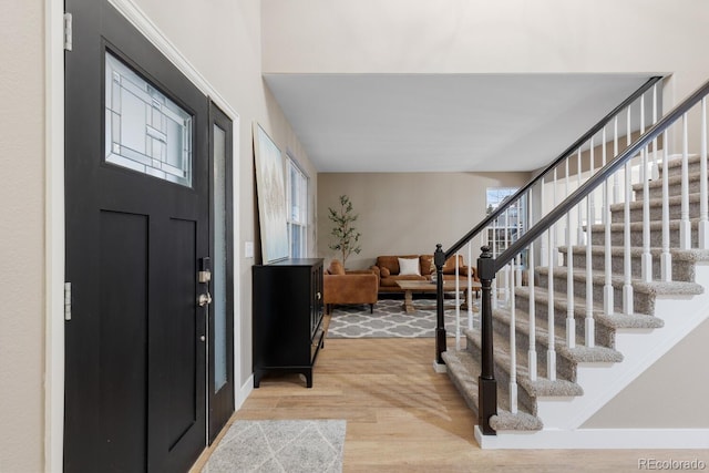 foyer entrance with light wood-type flooring, baseboards, and stairs