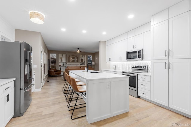 kitchen with light wood-style flooring, a kitchen island with sink, a sink, a kitchen breakfast bar, and appliances with stainless steel finishes