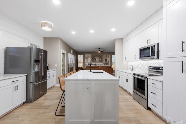 kitchen with an island with sink, a sink, white cabinetry, stainless steel appliances, and decorative backsplash