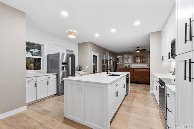 kitchen featuring appliances with stainless steel finishes, white cabinetry, light wood-style floors, and a sink