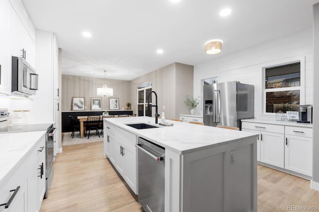 kitchen featuring an island with sink, a sink, light wood-style floors, appliances with stainless steel finishes, and white cabinets