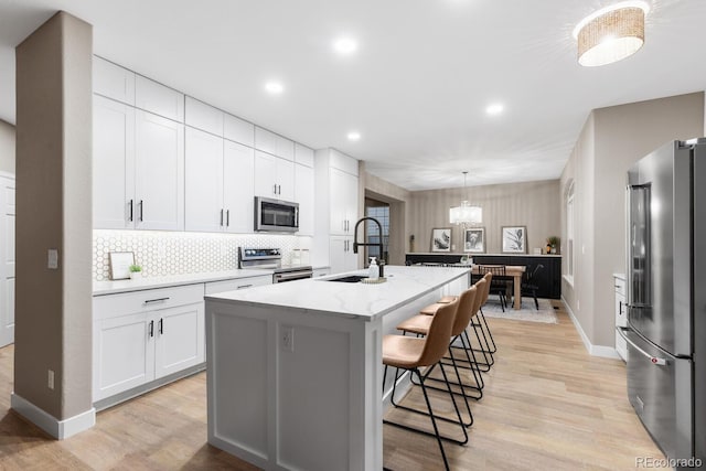 kitchen with a center island with sink, appliances with stainless steel finishes, a kitchen breakfast bar, white cabinets, and a sink