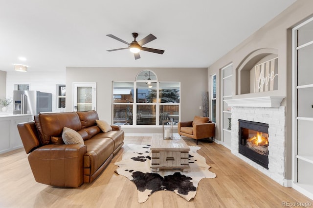 living area featuring a brick fireplace, light wood-style floors, and ceiling fan