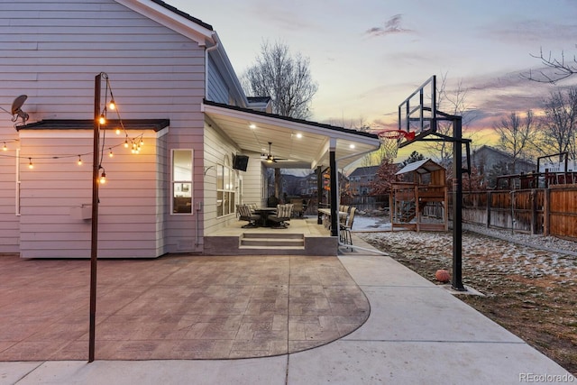 patio terrace at dusk featuring a playground, a ceiling fan, and fence