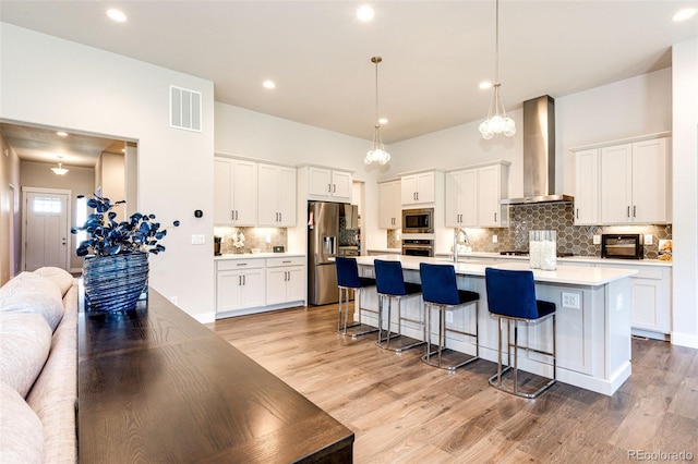 kitchen with light hardwood / wood-style floors, stainless steel appliances, wall chimney exhaust hood, pendant lighting, and white cabinets