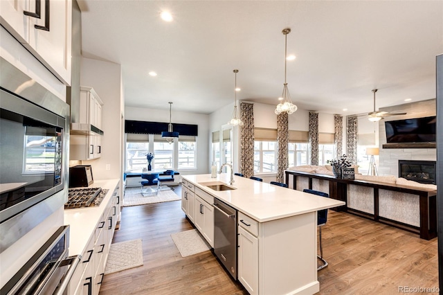 kitchen featuring a kitchen island with sink, hanging light fixtures, sink, white cabinets, and appliances with stainless steel finishes